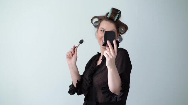Young woman in curlers rollers on hair doing makeup with brush, Beautiful girl