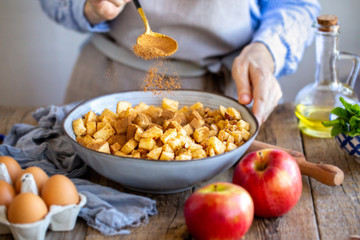 Add a spoonful of cinnamon to the filling of the cake. Cinnamon for apple strudel. Sliced ​​apples with raisins and cinnamon. Cooking a pie. Apple pie. Cinnamon flies in a bowl with apples
