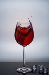 A glass of red wine and a splash from falling ice with a reflection.