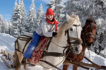 Portrait of a young pretty girl riding horseback riding a big white horse in an awesome snowy winter landscape