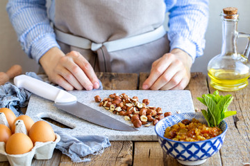 Grinds hazelnuts. A cook grinds a nut on a board with a knife. Hazelnuts on the board. stuffing with cinnamon, nuts and raisins for strudel. Cook at home. Ingredients for the pie.
