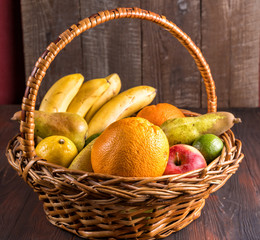 Fresh fruits in a basket on wooden table.