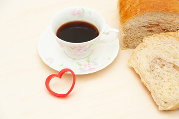 Homemade Brazilian bread sliced next to a cup of coffee and a red heart shape object. Isolated on light wooden background. Copy space. Concept: Celebration of Mother's Day and Valentine's Day.