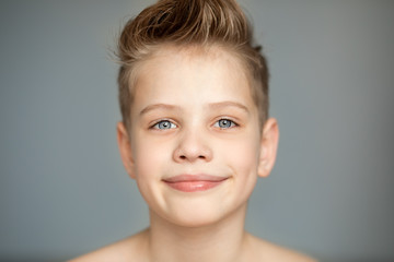 cute boy emotionally stretches his lips into a smile. A freestanding young man on a gray background smiles broadly. Eyes shine with happiness.