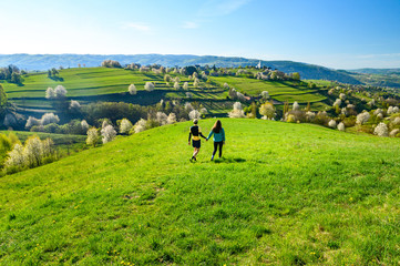 Fototapeta premium Couple date in green spring blossom sunny landscape. Rural scenery and church in background