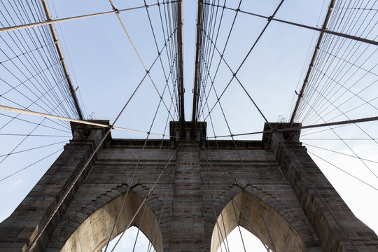 Brooklyn Bridge, photo from inside the bridge, perspective of one of the arches with the cables creating geometric shapes in the sky, in the middle you can see the US flag, photographs of New York