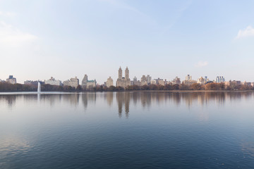 Fototapeta na wymiar New York City skyline from one end of a Central Park lake, the water reflects the skyline and the blue sky