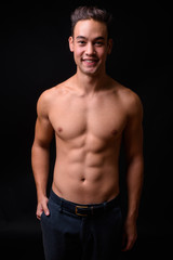 Young handsome multi ethnic man shirtless against black background