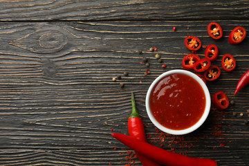 Chilli pepper and bowl of sauce on wooden  background, top view