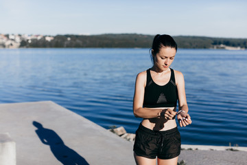 Fototapeta na wymiar Young sporty girl dressed in black listening to music in headphones during morning jog.
