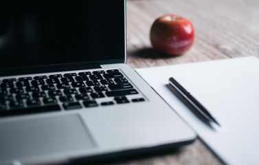 There are grey modern laptop, white paper A4, silver pen and red apple on the table. 