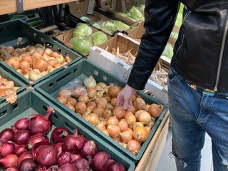 Man choosing onion in store. Close up of man's hand looking for good vegetables on store counter.
