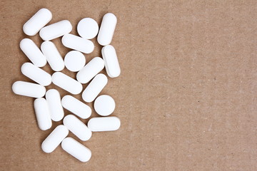 Pills for a headache - scattered white tablets on cardboard background