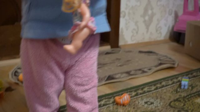 little girl puts toys in a box,girl in her hands holds a doll and puts it in a box, at home a little girl brings toys after playing