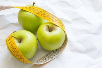 Closeup fresh green apples fruits with measuring tape isolated on white background. Slim diet and eating for healthy.