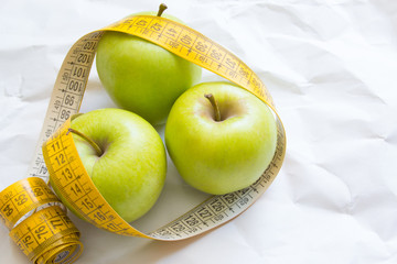 Closeup fresh green apples fruits with measuring tape isolated on white background. Slim diet and eating for healthy.