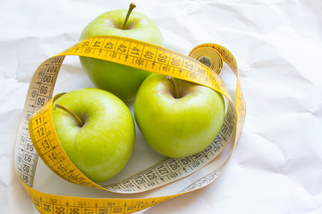 Closeup fresh green apples fruits with measuring tape isolated on white background. Slim diet and eating for healthy.