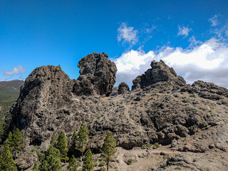 Lavafelsen Gebirge bei blauem Himmel mit Weißen Wolken  im Vordergrund Bäume