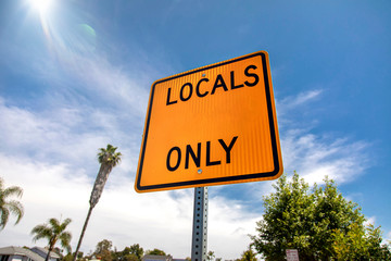 Yellow and black square road sign in neighborhood reading Local Access Only agasint a blue sky with...
