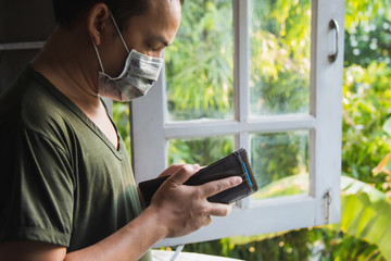 Close up Asian man in green casual shirt wearing a flu mask looking at his wallet, he is standing...