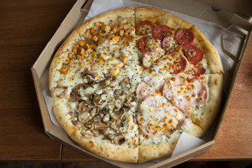 delivered to the house, chopped hot pizza in a cardboard box is on the table in the apartment. Pizza four seasons: with mushrooms, salami, pepperoni,  chicken and ham.
