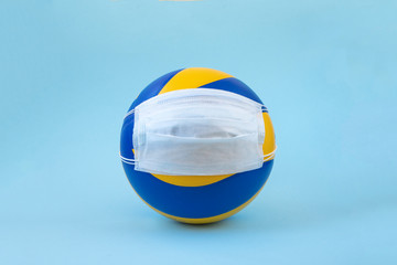 Volleyball ball in a medical mask on a blue background. Coronavirus stops volleyball games. Covid-19 stops sports. Coronavirus sport. Volleyball ball with surgery medical mask. Copy  space