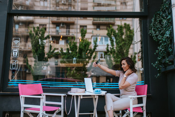 A beautiful young caucasian woman taking selfies in a cafe garden
