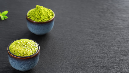 Matcha green tea in a blue ceramic bowl, next to a bowl is matcha green tea powder. Travel, Japanese tea ceremony, black stone background with copy space, close-up