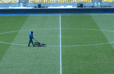 Worker mowing lawn on the soccer field of the stadium