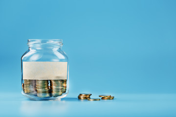 A glass jar with coins and a sticker with free space for text, on a blue background.