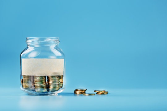 A glass jar with coins and a sticker with free space for text, on a blue background.