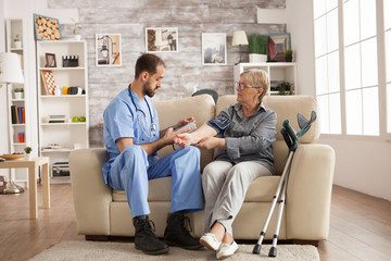 Fototapeta premium Male doctor with stethoscope around his neck taking the blood pressure of senior woman in nursing home.