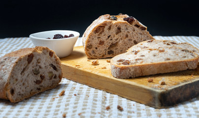 Slices of homemade bread with raisins, walnuts, spices and chopped nuts on beige and white tablecloth with a small white bowl of raisins
