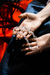 Female hands holding glass beads over a table, covered with blue and red cloth. Jewelry shimmers and glistens in the sun