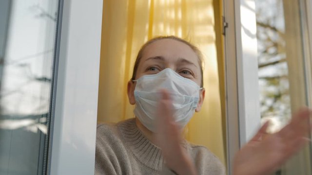 Woman in protective mask on the face looking in through the open window applauds