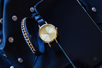 Watch with a leather strap and chains. Round dial next to a mobile phone in black and blue. Place for text. Background.