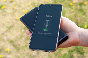 Smartphone charging without cable from induction power bank in the woman hand. Modern technology concept.