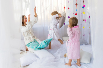 Young woman have fun with the children playing with pillows on the bed in the bedroom. Stay home and family concept.