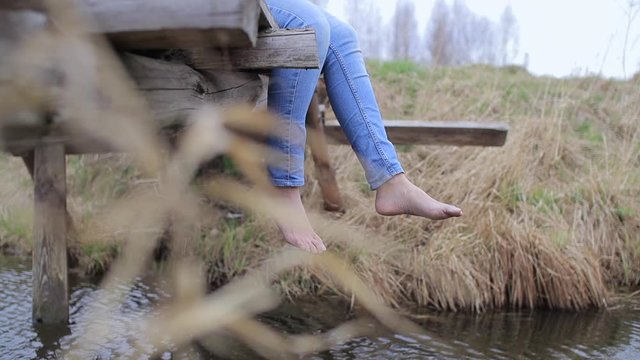 Woman legs in jeans without shoe dangling from old wooden bridge