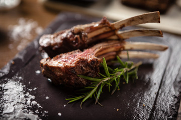 Grilled lamb chops with a branch of rosemary on a black board. Delicious healthy gourmet meat food...