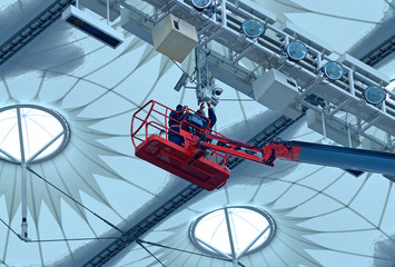 Workers repair sports lighting fixtures of the stadium using boom lift