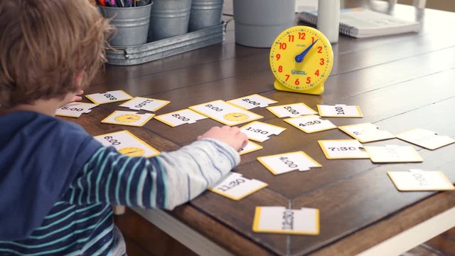 Little Boy Looking At Time Illustrations And Studying Clock. Blond boy is sitting at home during covid-19 pandemia and he is learning how to tell time.