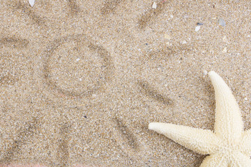 Fototapeta na wymiar Starfish on golden ocean sand, near the sun drawn by a child on the sand. The concept of tourism, leisure and travel, vacation by the sea. Copy space. Flat lay. Top view.