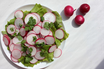 Fresh radish, lettuce and parsley salad in white plate on a white wooden background with copy space. Top view.
