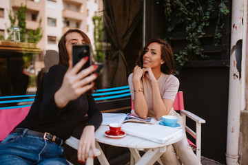 Two beautiful caucasian women are sitting in a cafe and taking selfies