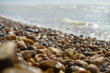 Low angle narrow point of focus on pebbles with sea and shoreline blurred in background.Sunny day and Bokeh.Image
