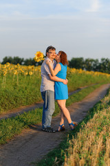 Adult couple cuddling in a field with sunflowers at sunset.