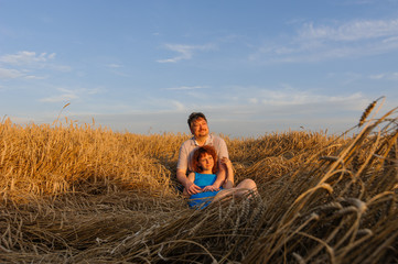 Naklejka na ściany i meble An adult farmer and his wife spend time together. A couple is sitting in a wheat field and watching the sunset.