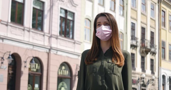 Young woman in pink protective medical mask walks down to the street. Thinking about safety life, N1H1 coronavirus, virus protection, pandemic.