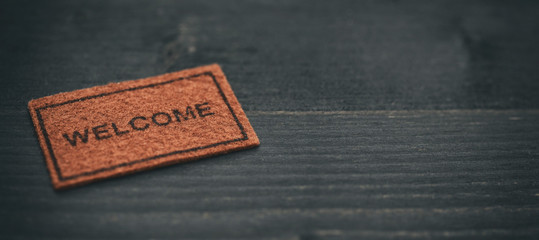 Old Welcome door mat on black wooden background